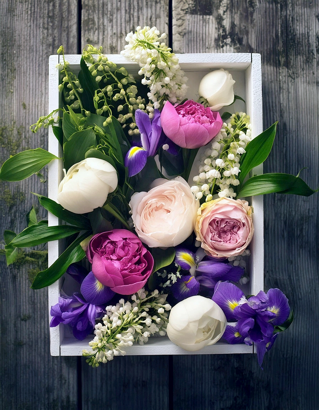 Wooden box filled with roses, irises, and lily of the valley flowers.