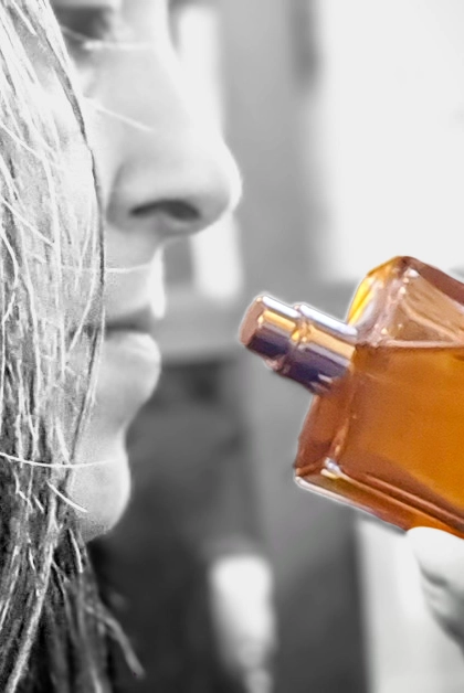 A black and white profile of a woman sniffing a colorful perfume bottle.