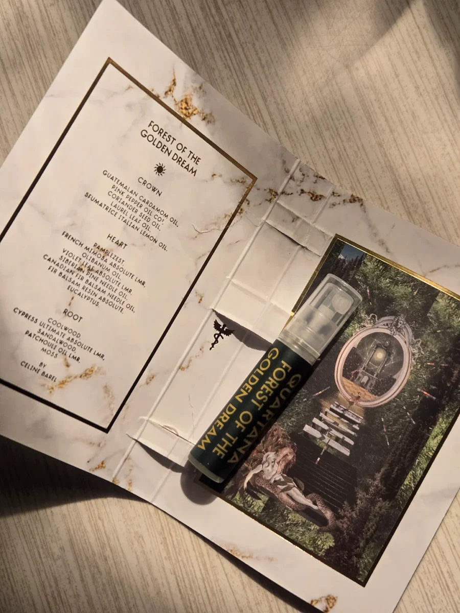 An open sample card for Quartana Forest of the Golden Dream, showing the list of fragrance notes on the left, the spray vial in the center, and the artistic imagery on the right.