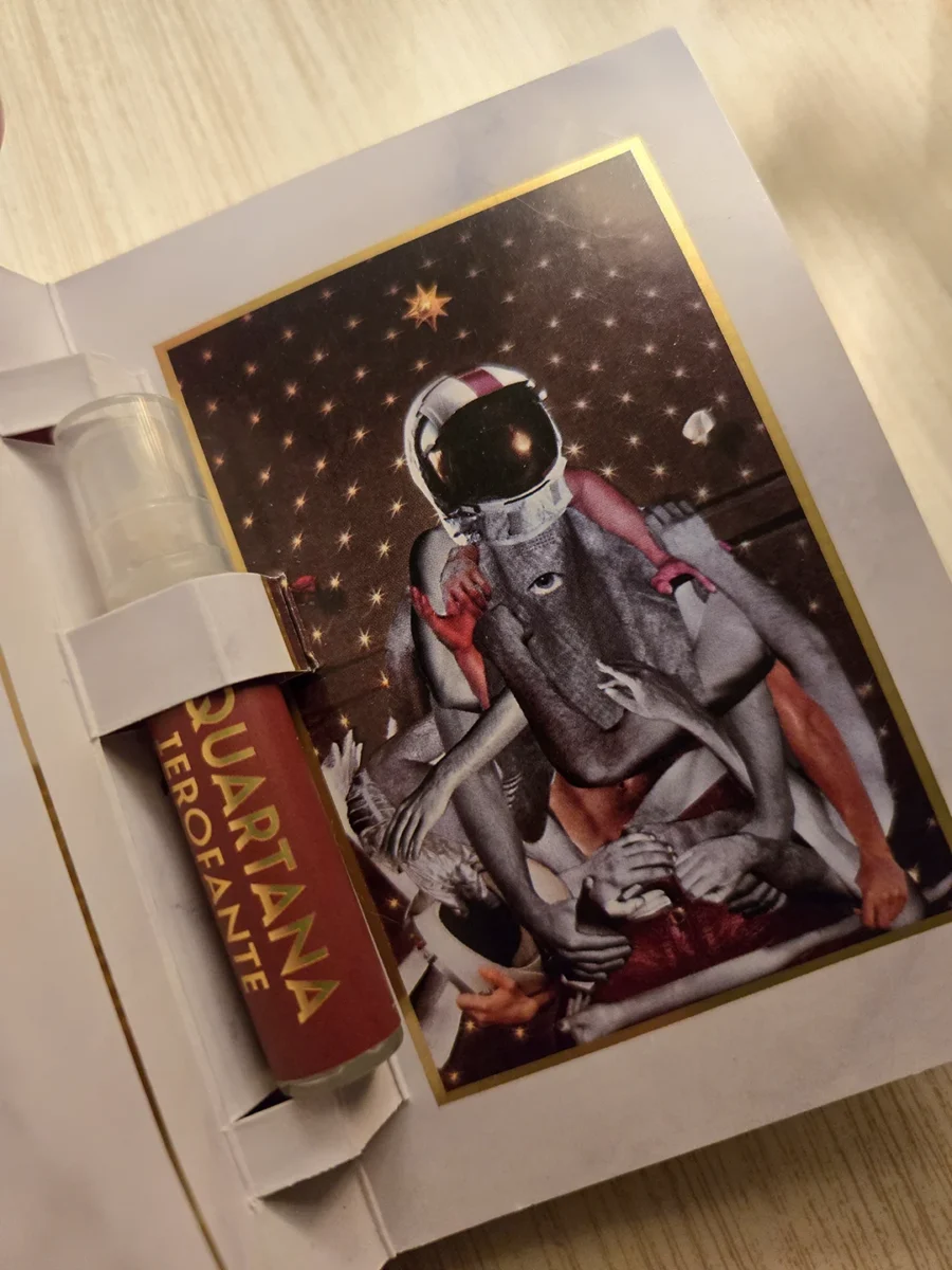 A sample vial of Parfums Quartana Ierofante resting in its sample card holder in front of surreal collage-style artwork.