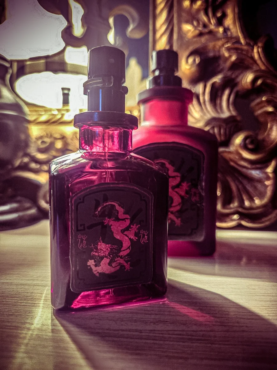 Two red Lucky Number 6 perfume bottles, one clear and one matte, sitting on a wooden surface with a warm glow from a background lamp.