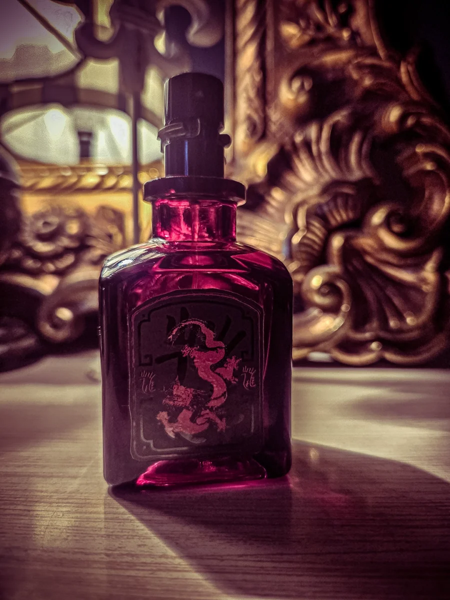 Close-up of the transparent red Lucky Number 6 perfume bottle with a black dragon label, illuminated by sunlight and a warm lamp.