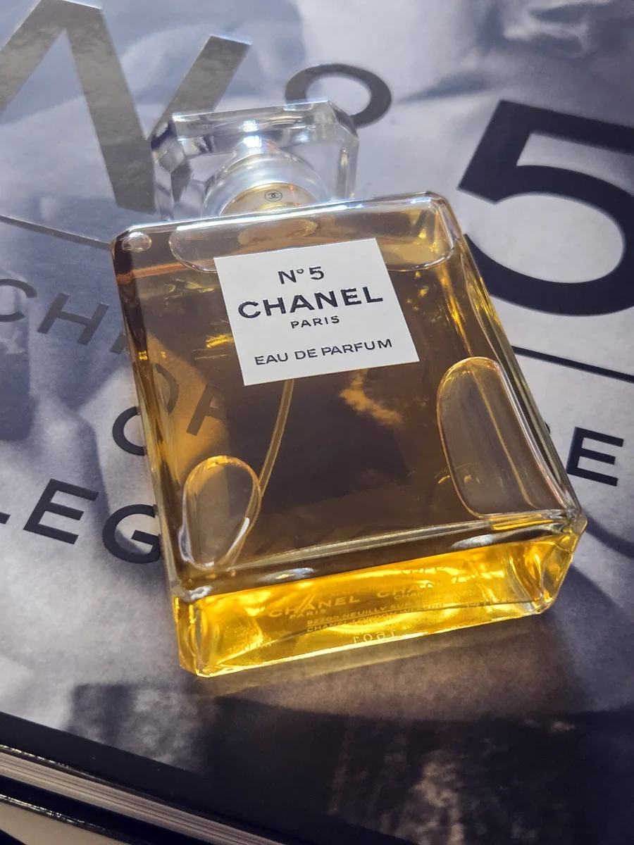 Chanel N°5 Eau de Parfum bottle resting on open pages of the Abrams book, "The Story of Chanel N°5."