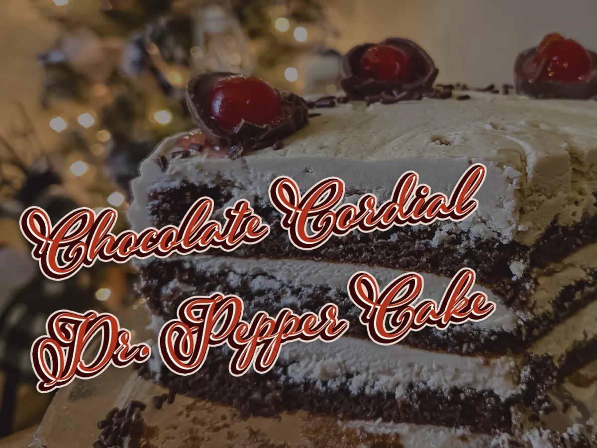 A close-up cross-section of a three-layer Chocolate Cordial Dr. Pepper Cake with creamy frosting, topped with halved chocolate cordial cherries and maraschino cherries against a festive holiday background.