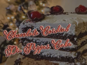 A close-up cross-section of a three-layer Chocolate Cordial Dr. Pepper Cake with creamy frosting, topped with halved chocolate cordial cherries and maraschino cherries against a festive holiday background.